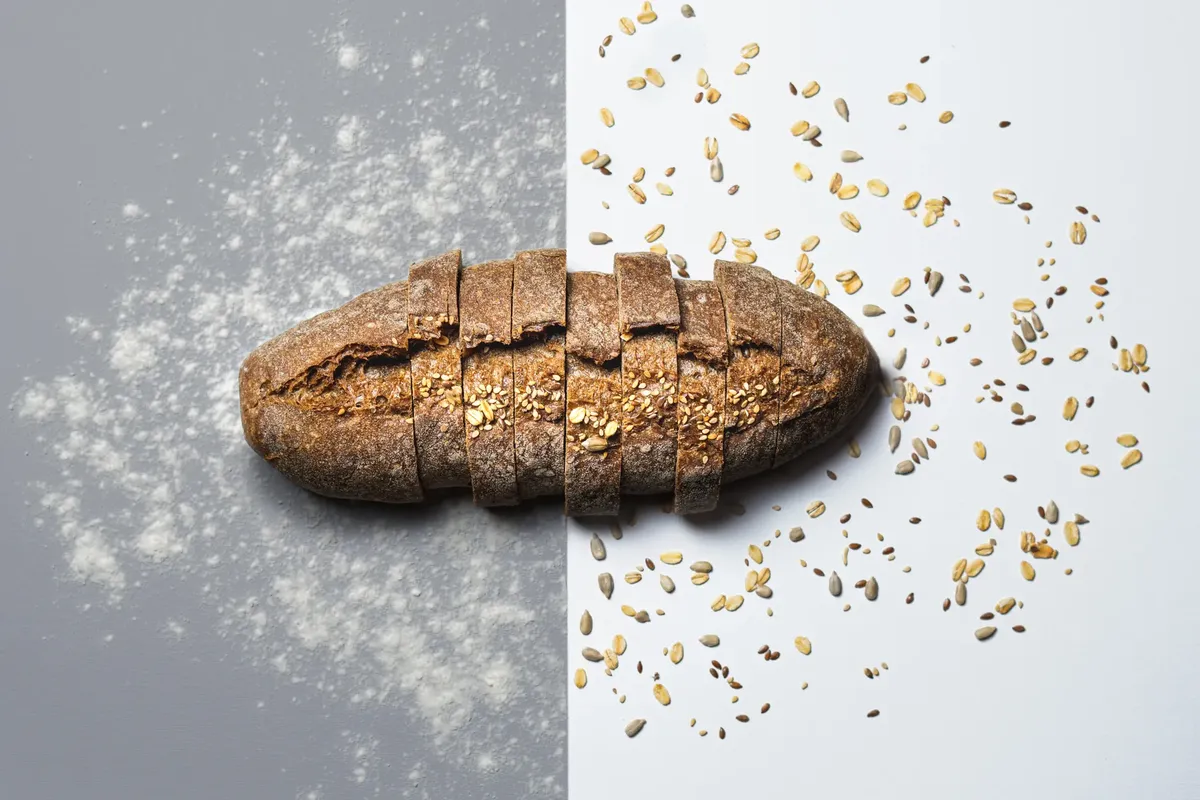 A rustic sliced loaf of bread with seeds on a contrasting gray and white background.
