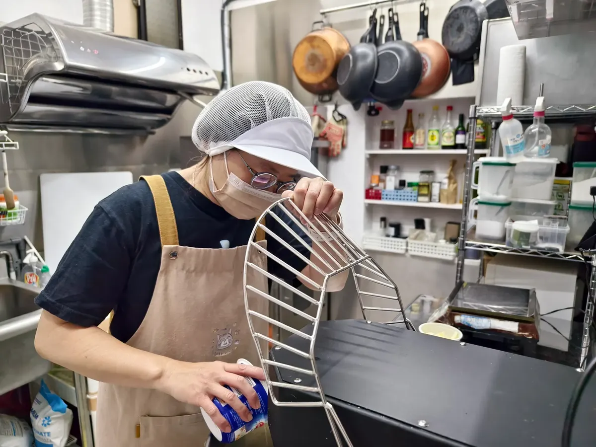 A chef in a kitchen apron and cap prepares equipment in a professional kitchen setting.