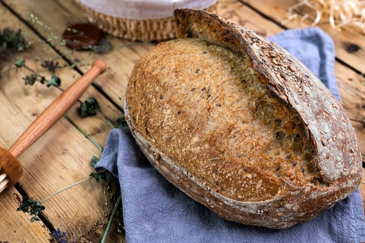 Freshly baked sourdough bread with seeds on a rustic wooden table setting.