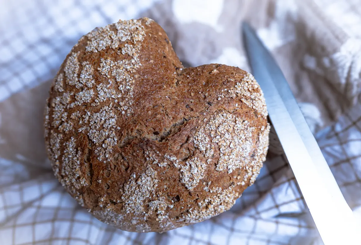 Close-up of heart-shaped rustic whole grain bread on a cloth with knife.