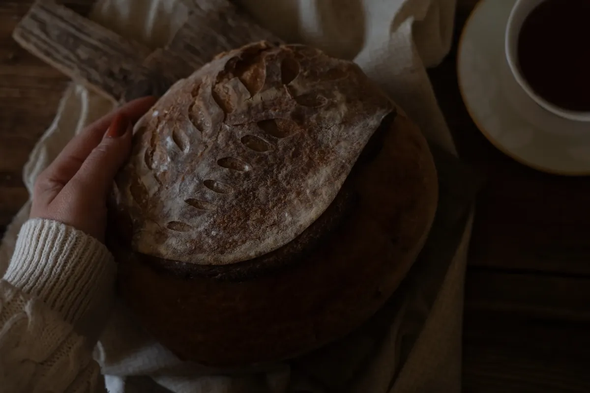 Close-up of a hand holding artisanal sourdough bread with a cup of coffee nearby.