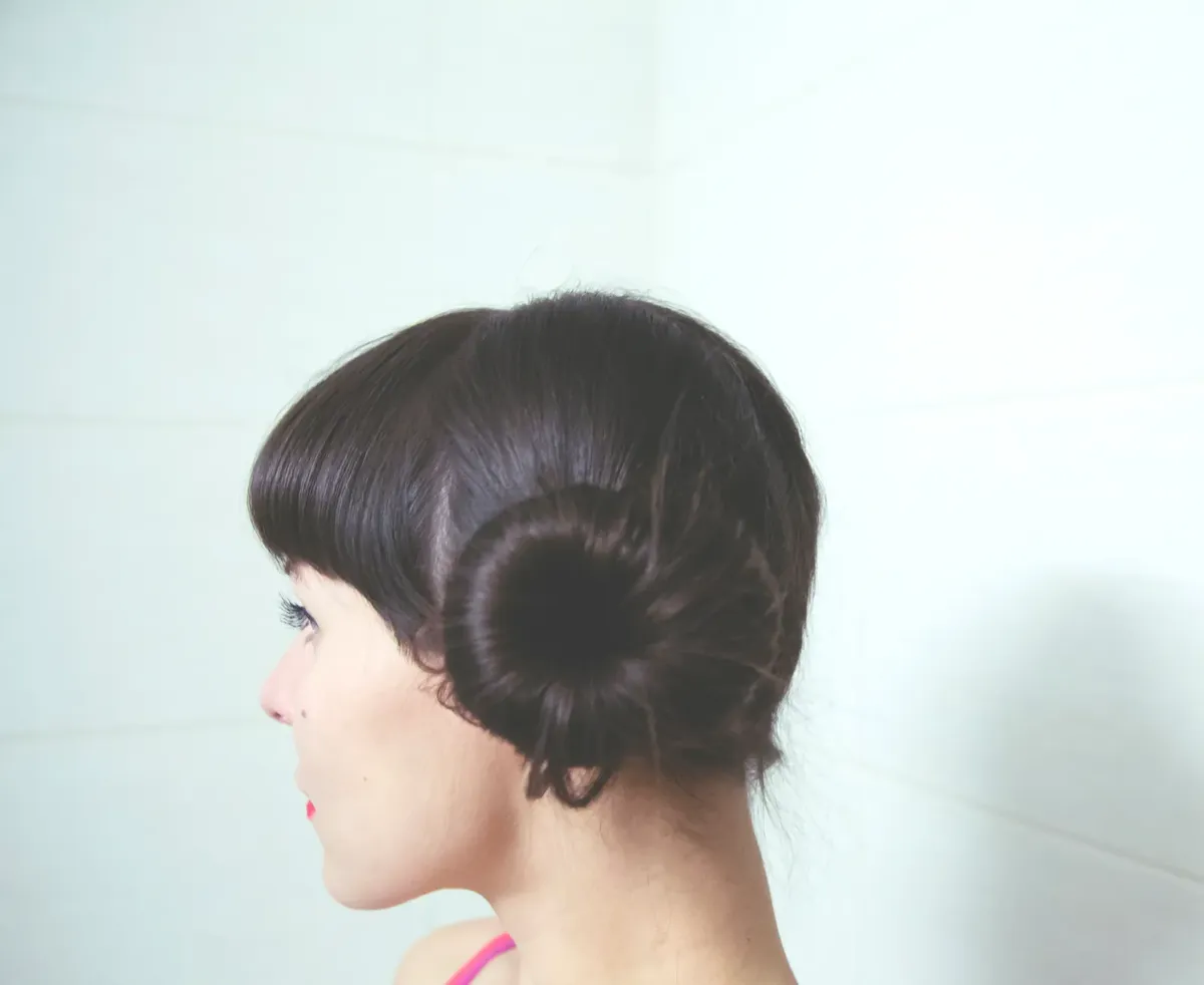Side view of dark haired female with bun on head standing against white tiled wall