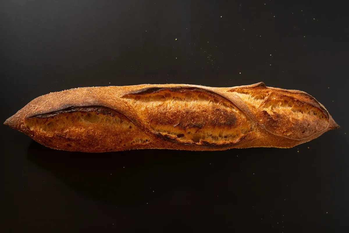 Close-up of a freshly baked artisan baguette displayed on a dark surface.
