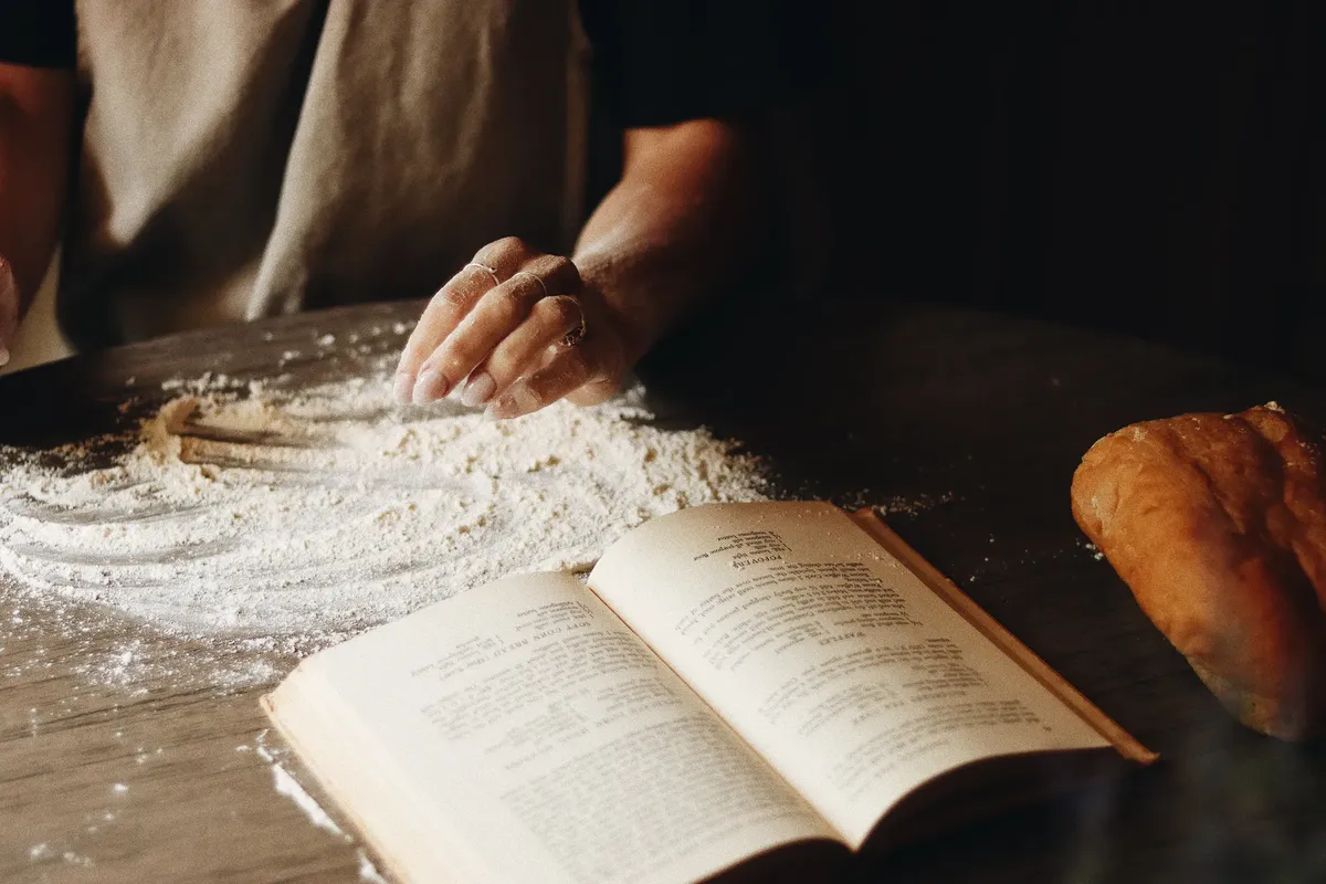 A close-up of hands shaping dough beside an open recipe book, capturing the art of home baking.