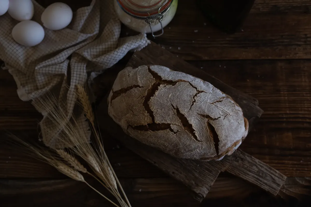 Artistic shot of homemade rustic bread with eggs and wheat on wooden table.