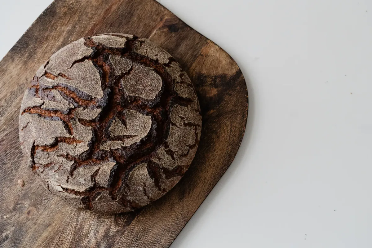 Top view of a rustic artisan bread on a wooden cutting board, highlighting its detailed crust.