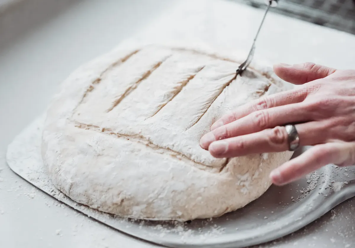 A detailed view of hands scoring bread dough for baking, showcasing artisanal bread preparation.