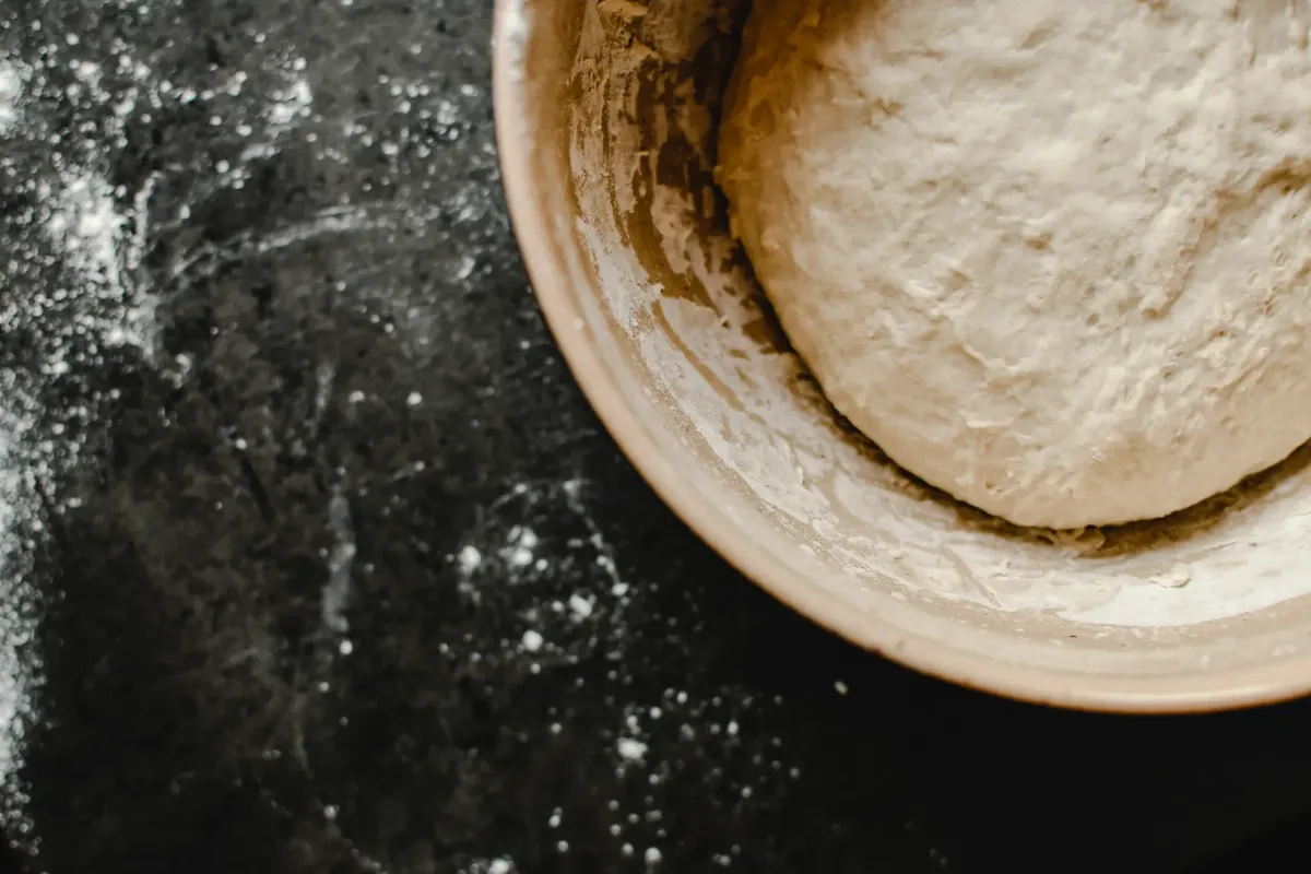 Aerial view of dough in a bowl on a floured surface, ready for baking.