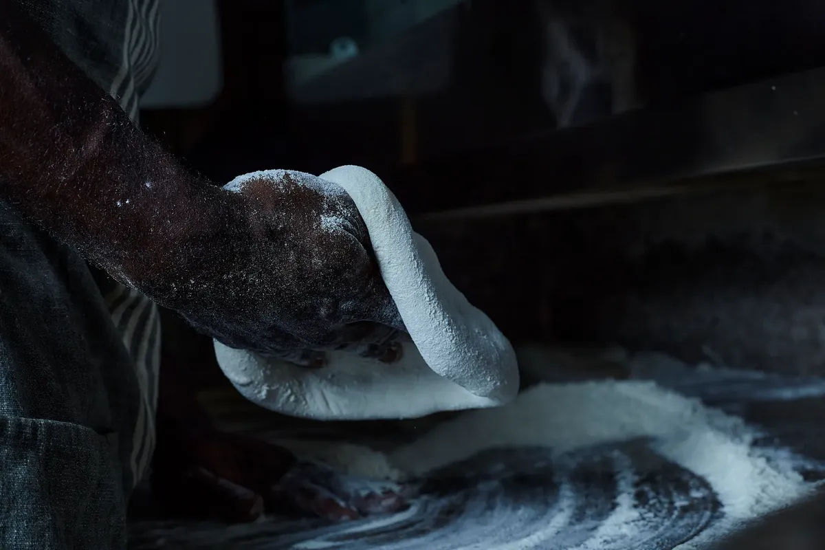 Close-up of a baker's hands kneading dough in a dimly lit kitchen setting.