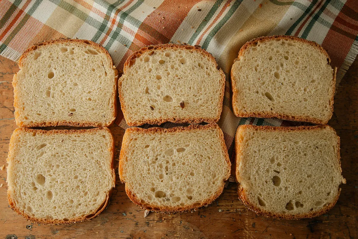 Six slices of fresh bread arranged on a wooden table with a plaid cloth backdrop.