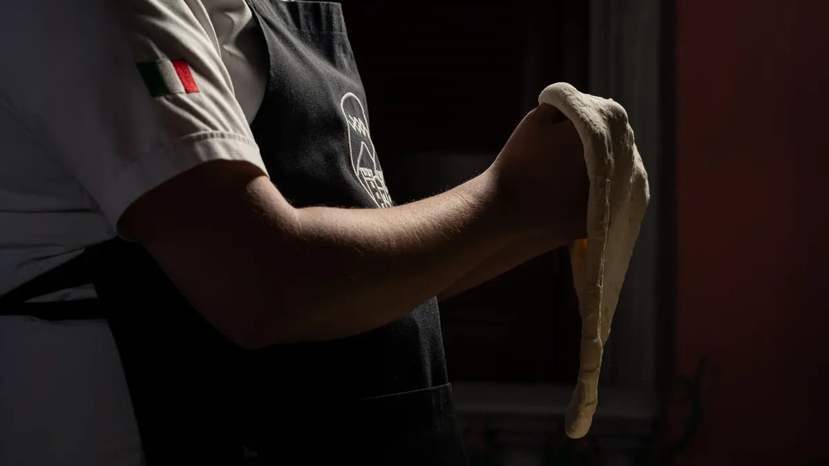 Close-up of a chef kneading pizza dough in a dimly lit kitchen, showcasing culinary skills.