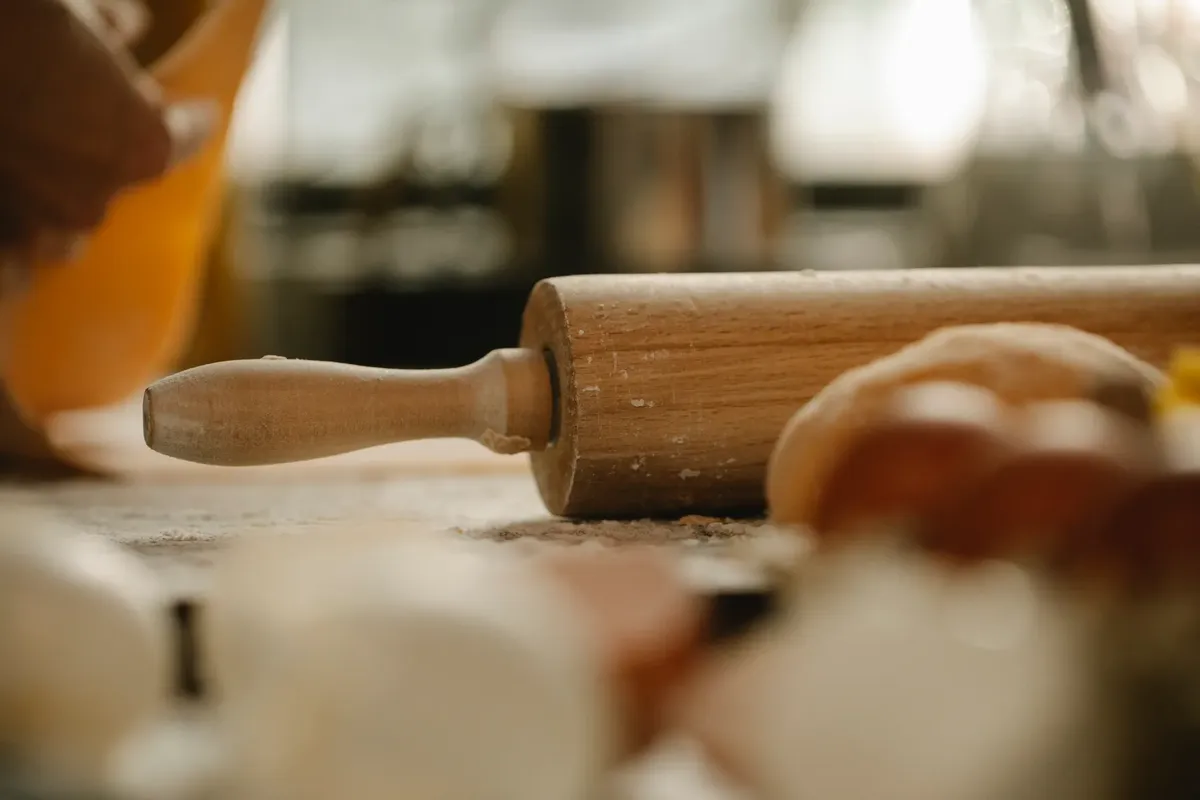 Crop anonymous cook with thin dough at table with wooden rolling pin and flour during cooking process at home