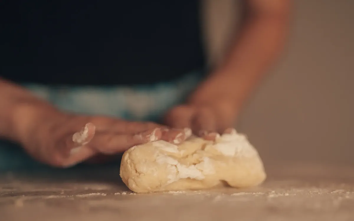 Hands kneading dough on a floured surface in a kitchen setting, focused on baking preparation.