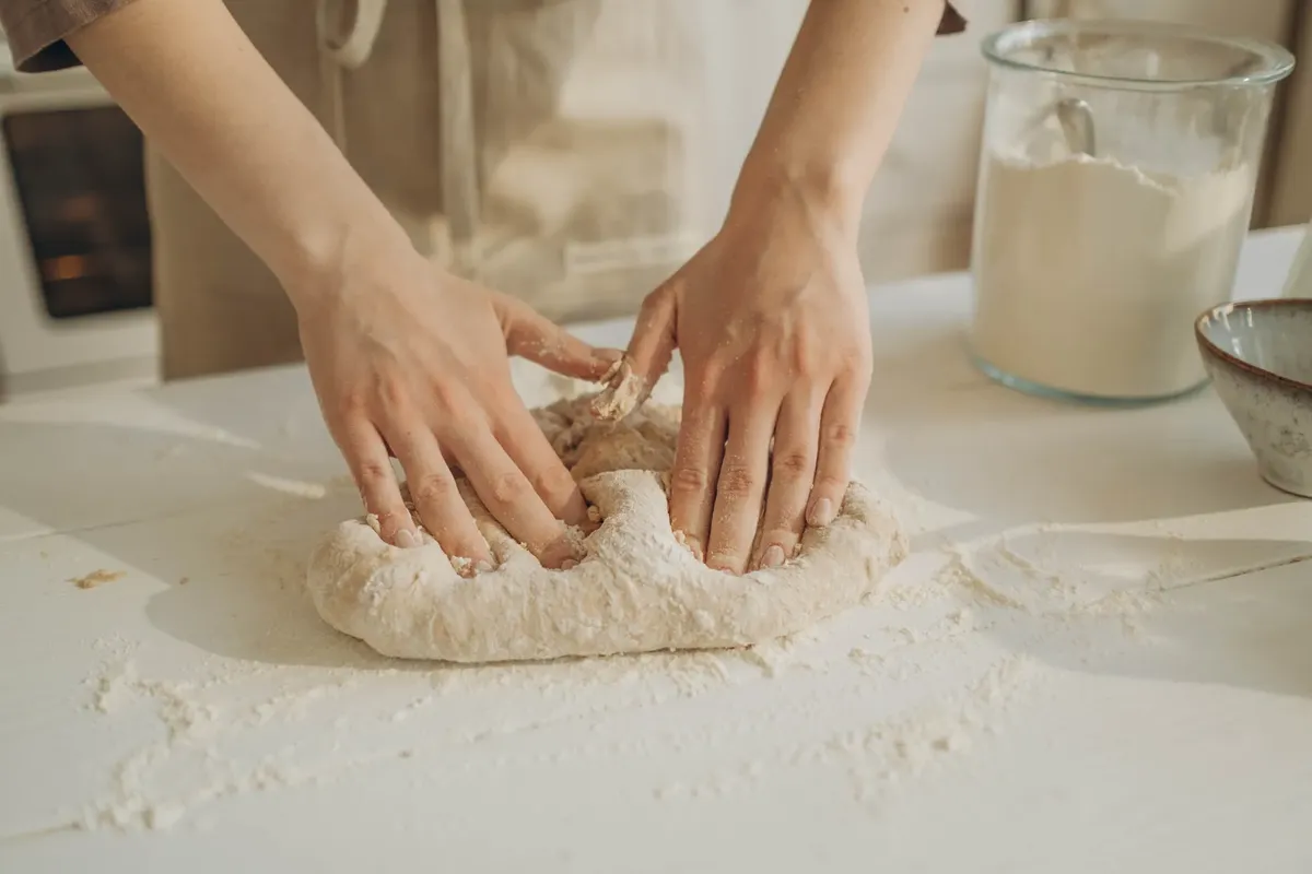 Closeup of hands kneading dough on a white table with flour, capturing the baking process.