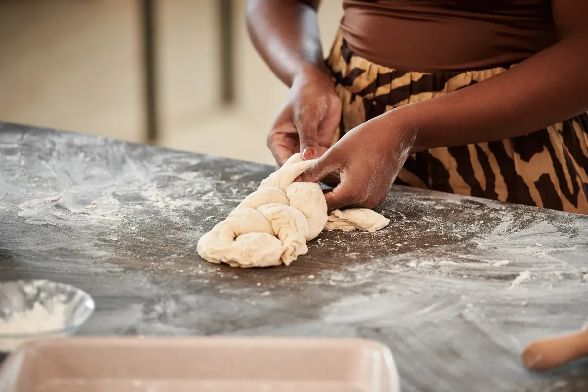 Close-up of hands kneading dough with flour on a kitchen surface, showcasing a baking process.